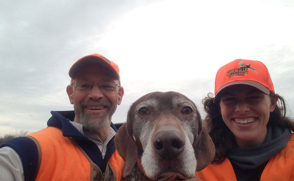 male and female hunters in orange taking a selfie with hunting dog