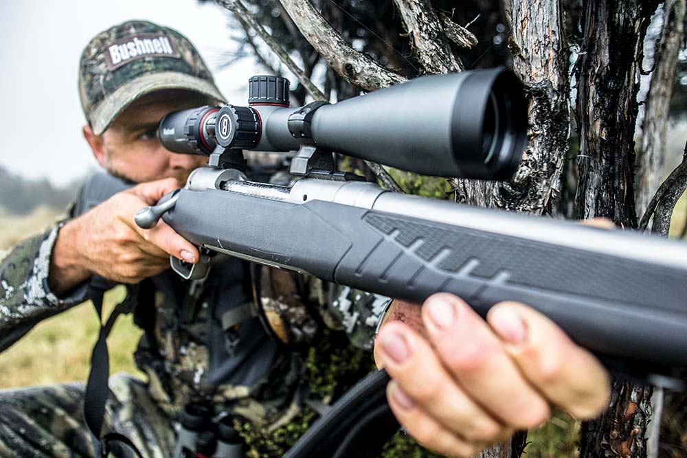 Hunter aiming a rifle fitted with a Bushnell scope.