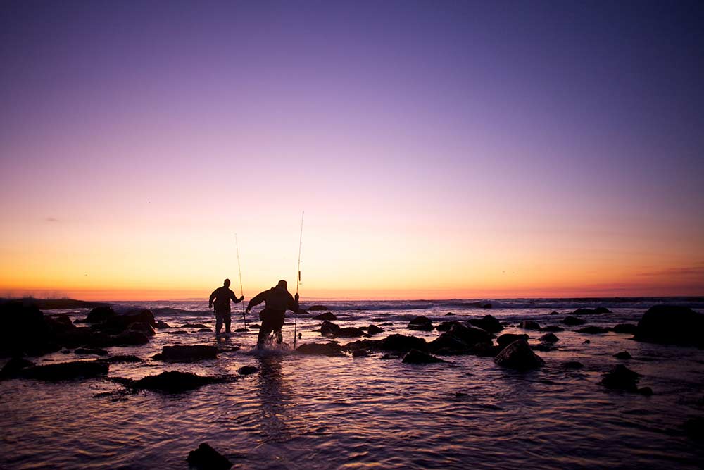 two anglers fishing shoreline at sunset