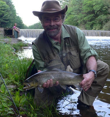 fisherman kneeling while holding a trout
