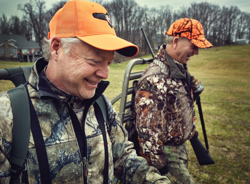 Two hunters smile and walk through a an open field.