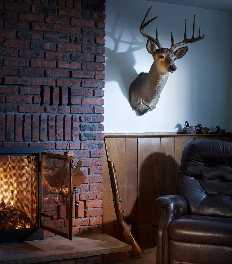 Deer mount in a living room next to a fire. 