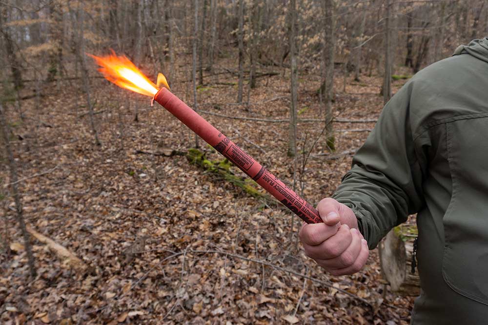 man holding a road flare in the woods