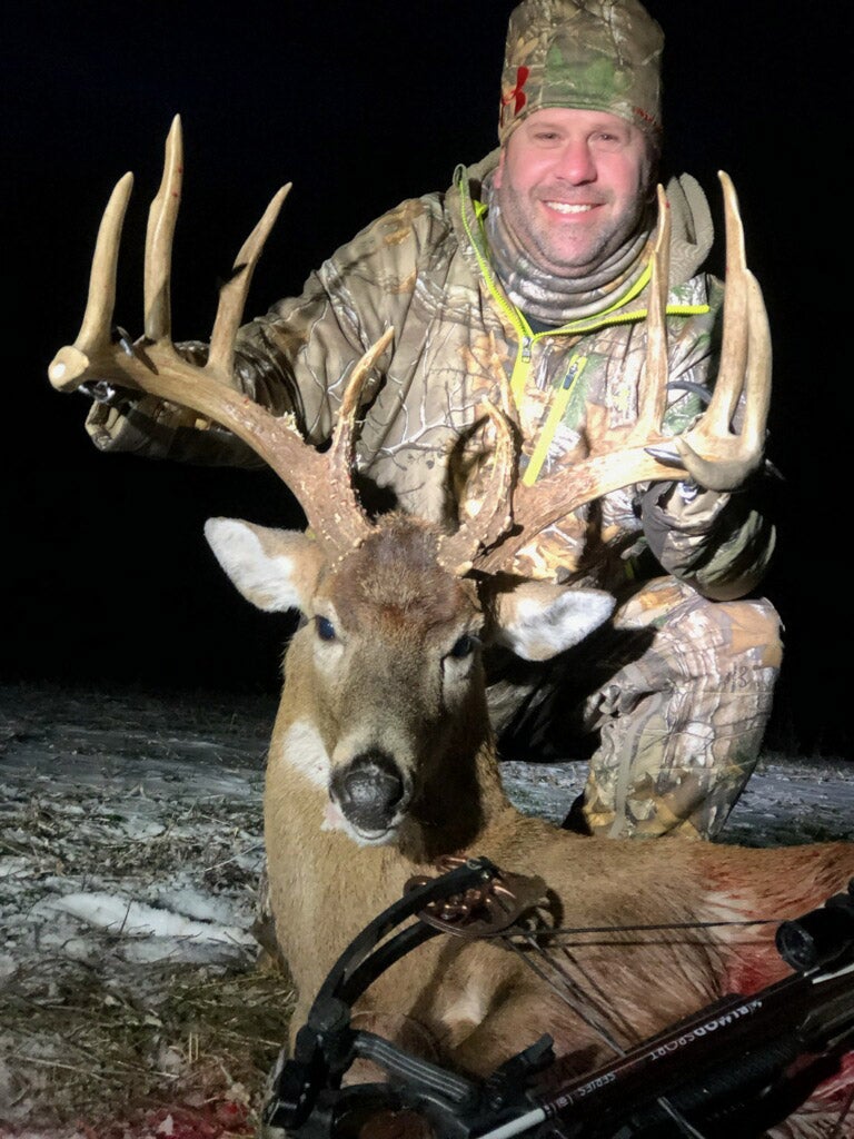 Jason holding up buck with crossbow at night