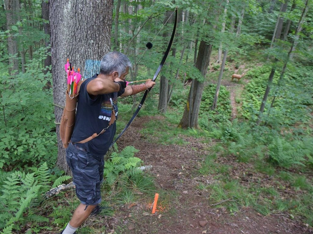 man aiming a bow and arrow in a forest