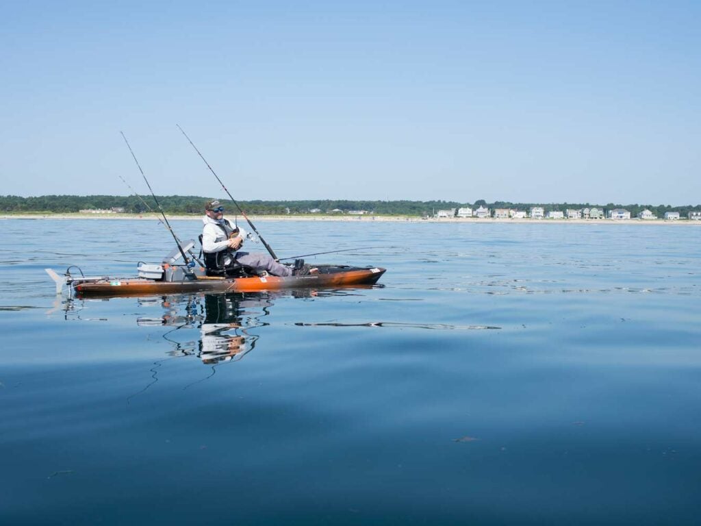 A fishing kayak with a motor attached to the stern glides across the water.