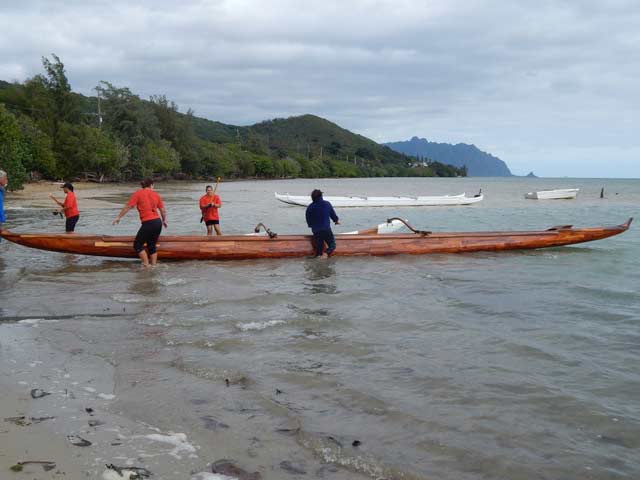 A team prepares to paddle a traditional wooden koa canoe.