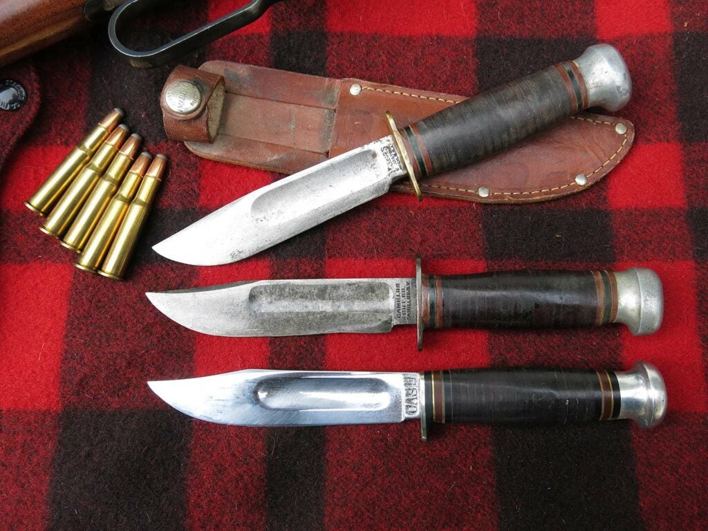 three antique hunting knives on a plaid backdrop