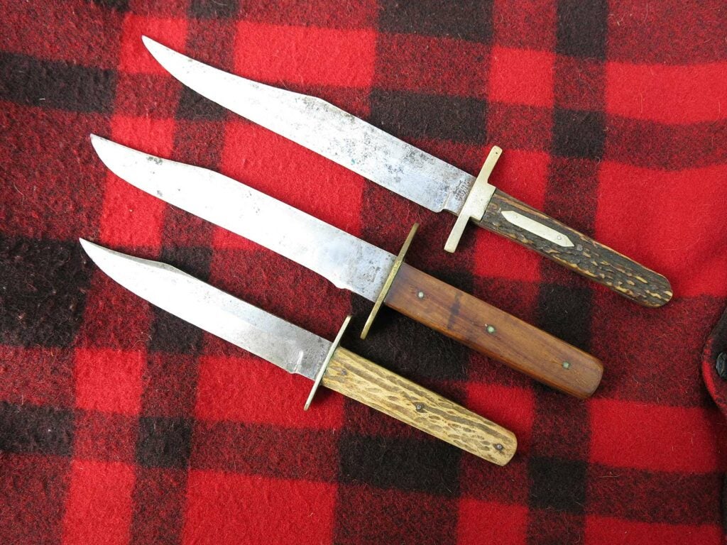 three antique hunting knives on a plaid backdrop