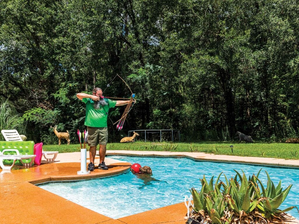 man testing a custom crafted bow by a pool