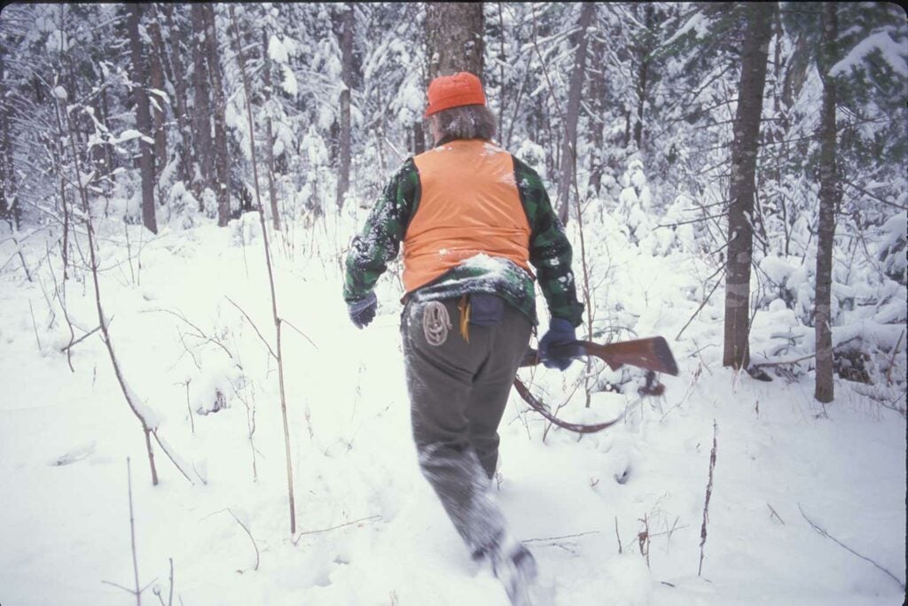hunter in orange walking through snowy woods