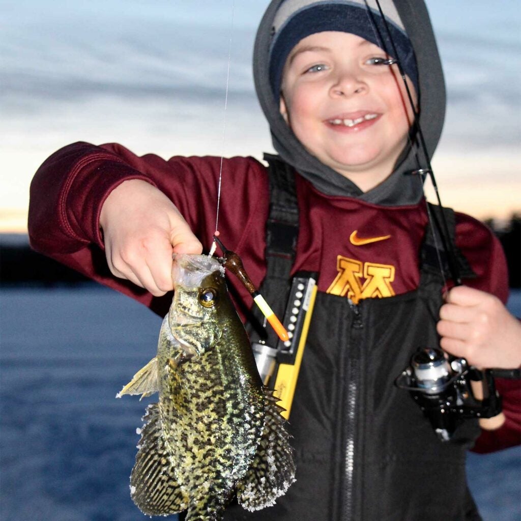 Young child holding up a fish caught from ice fishing.