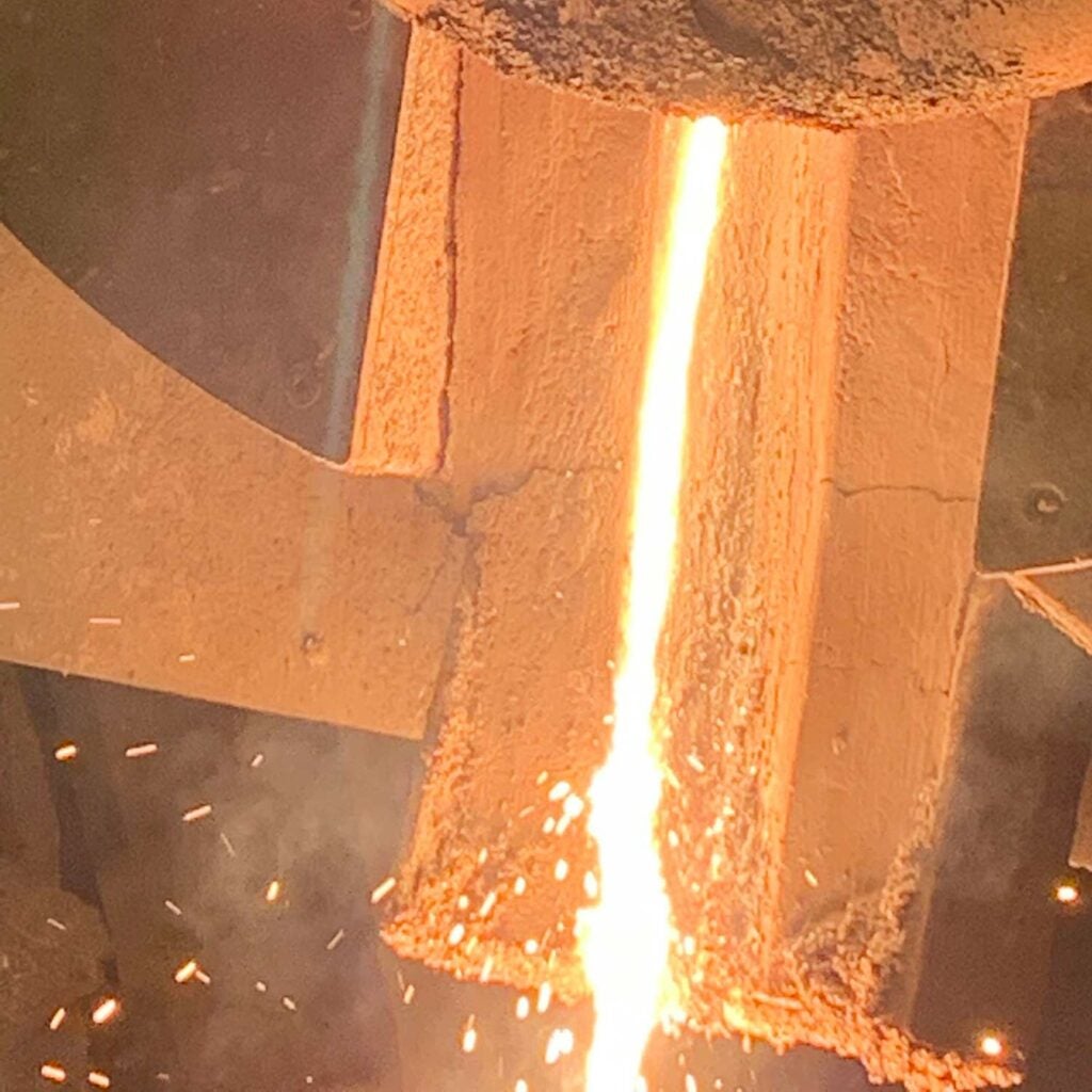 Molten metal being poured from the induction furnace into the tundish, a trough through which molten metal flows under vacuum (not shown).