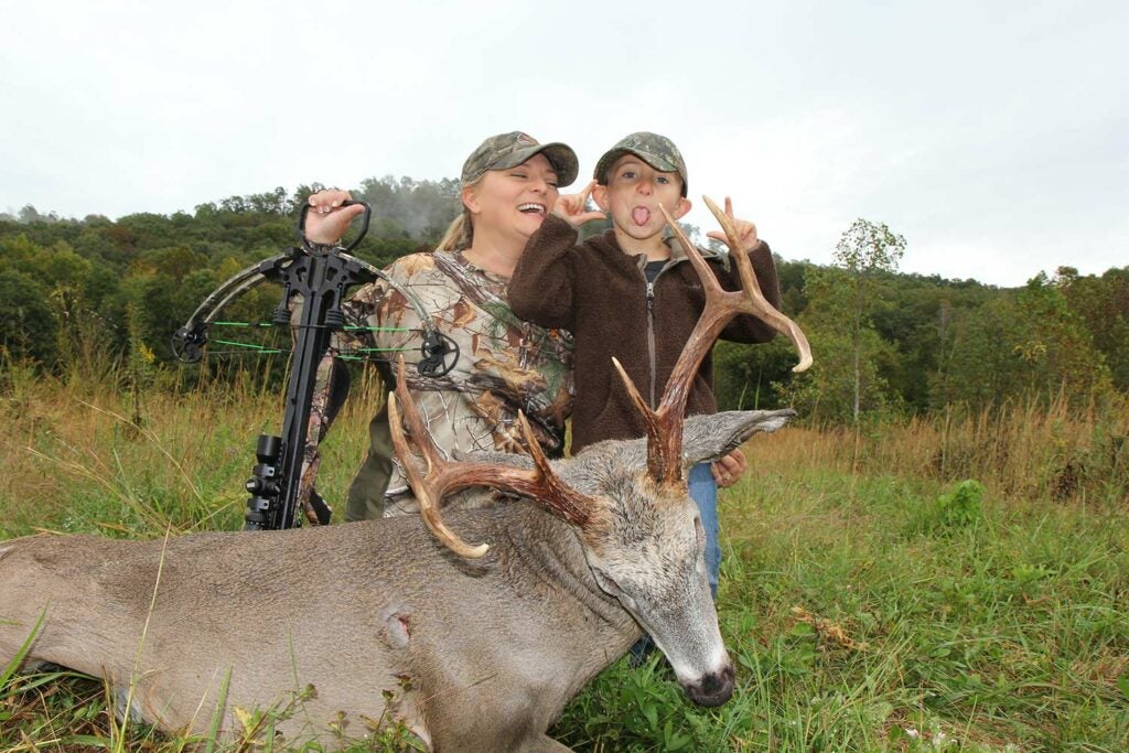 Mother and son kneeling behind a whitetail buck.