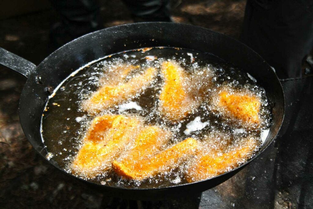 A cast iron skillet frying fillets of fish.