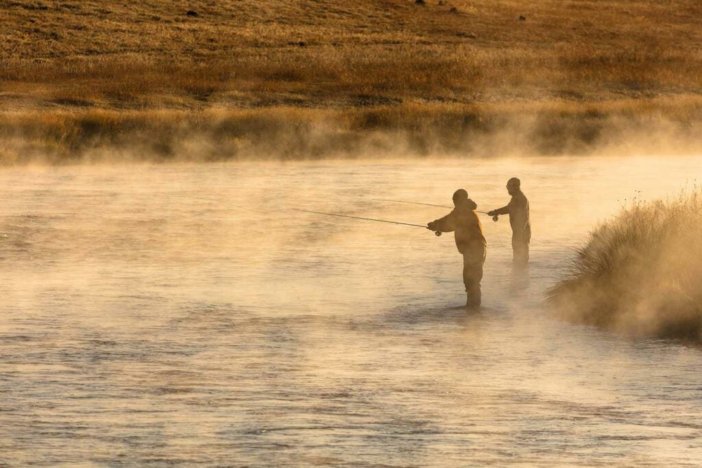 Two anglers fly fishing in the morning fog on a river.