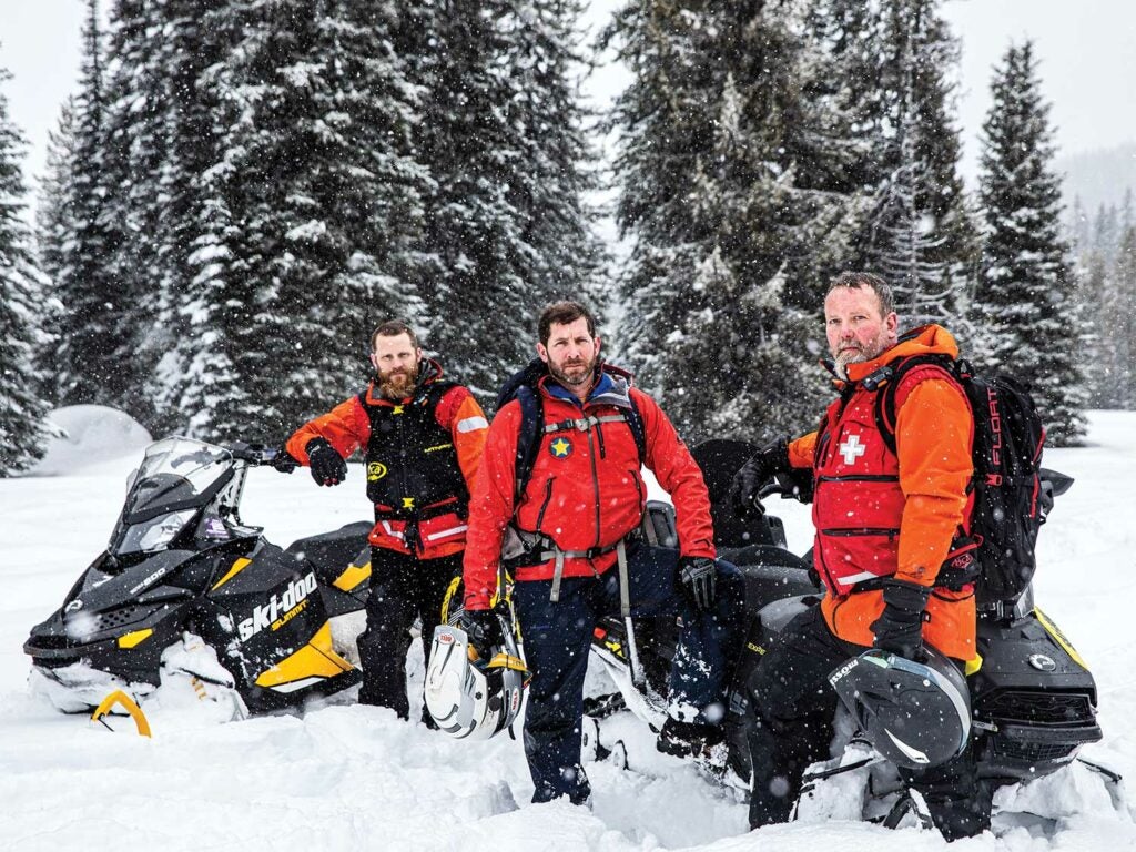 A search and rescue team standing beside snowmobiles.
