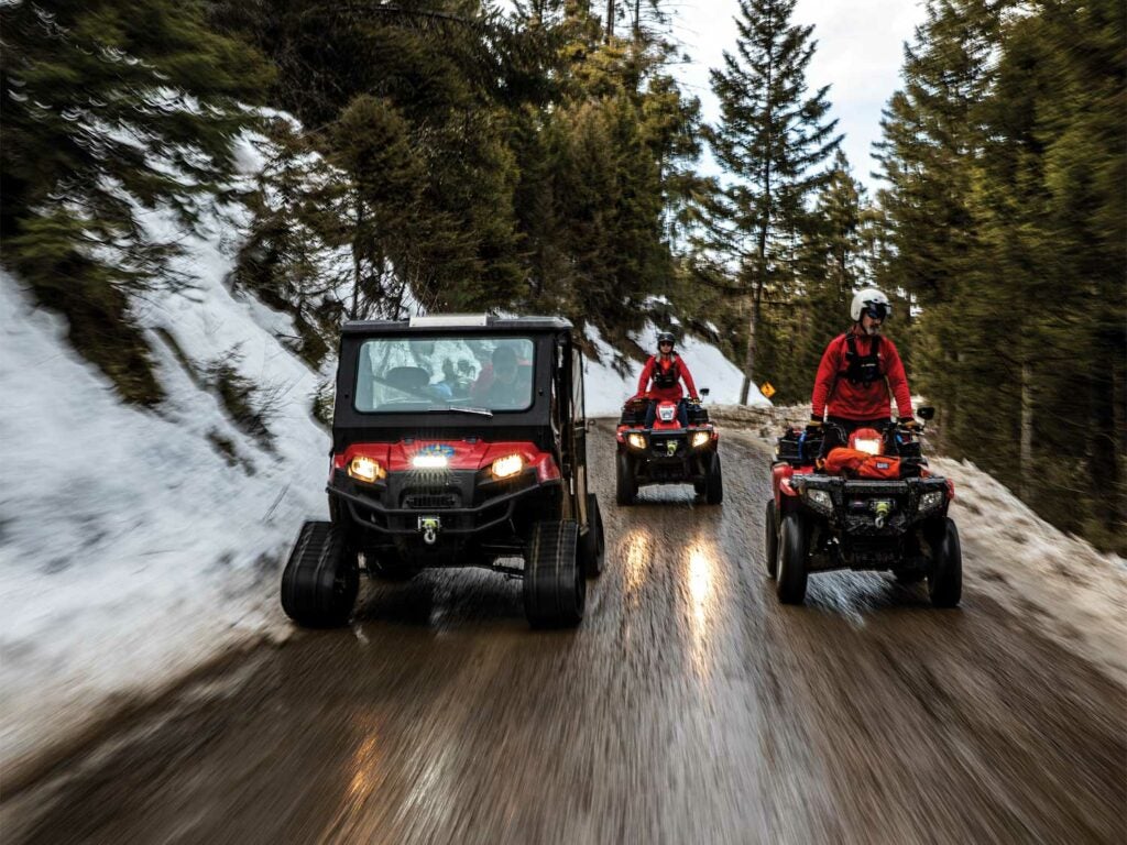 A team of search and rescue personnel drive a UTV and two ATVs down a road.