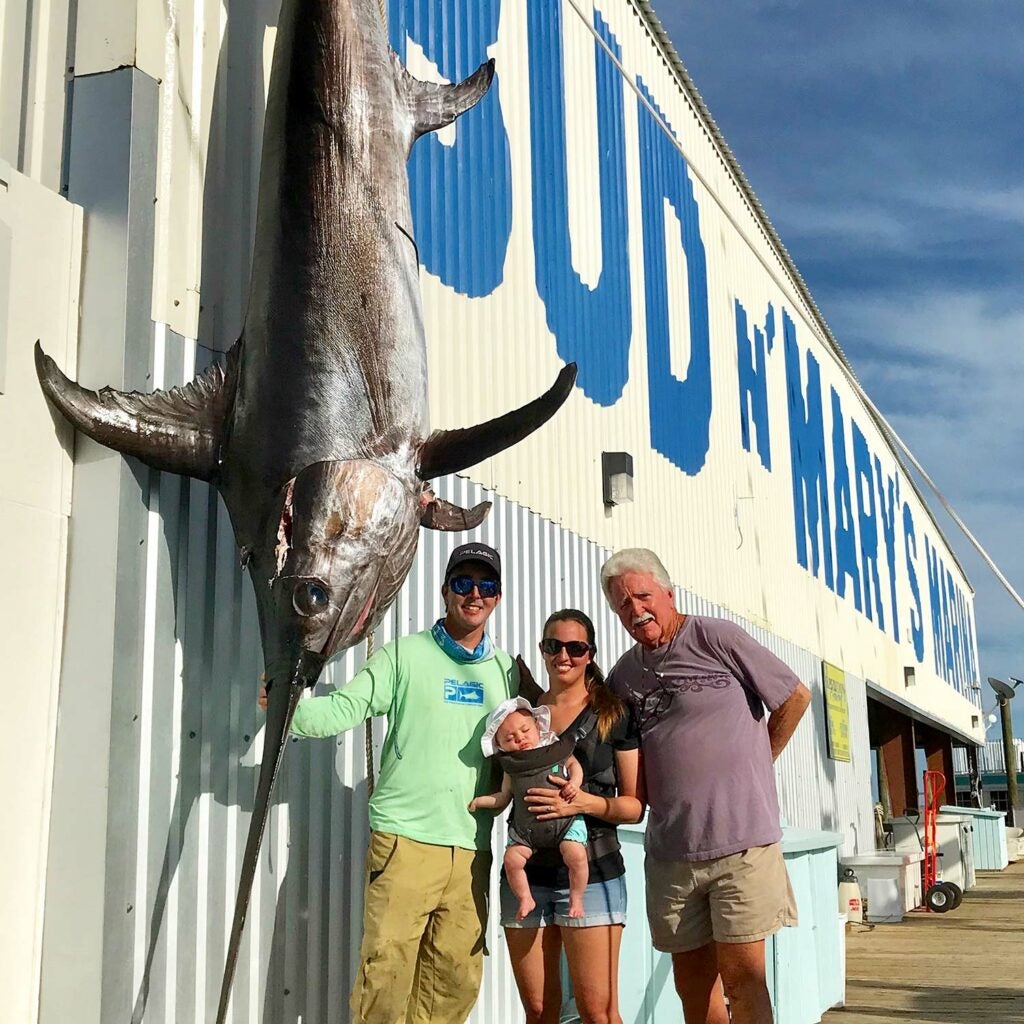 Three people stand beside a large swordfish.
