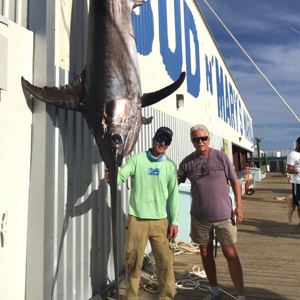 Two anglers stand beside a large swordifhs.