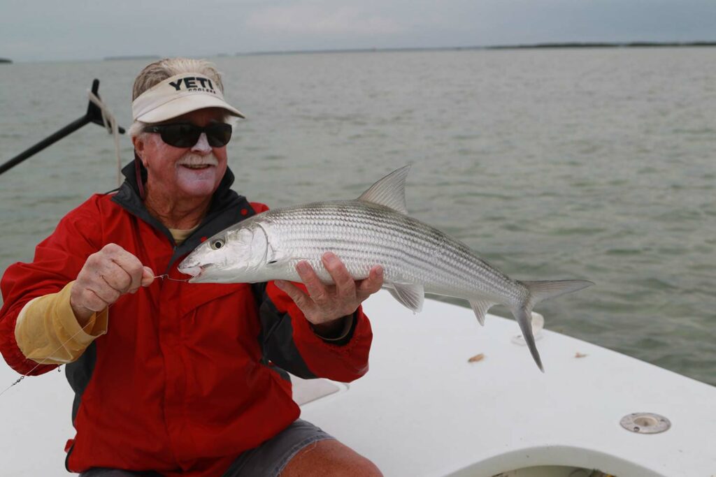 An angler in a red shirt holding up a bonefish.