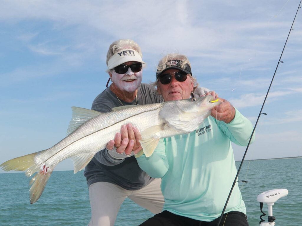 Two anglers hold up a large snook.