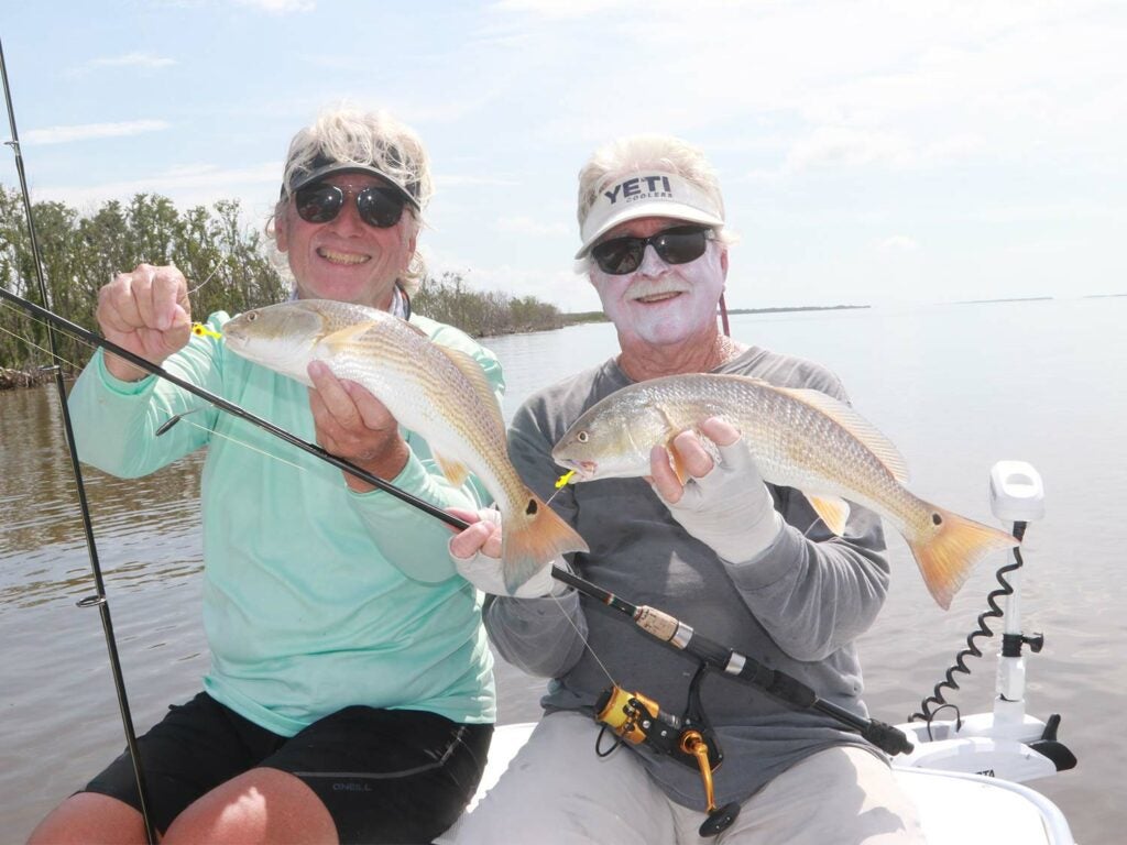 Two anglers in a boat holding up redfish.
