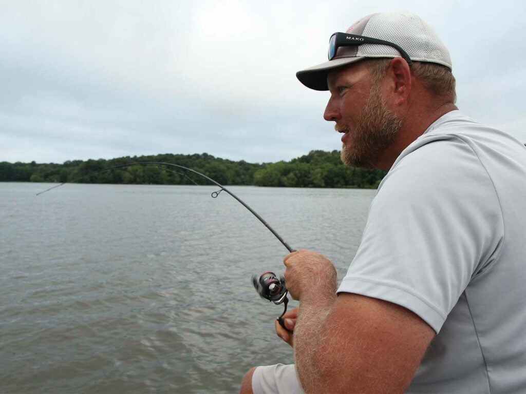 A bass fishing angler in a white shirt fishing in a lake.