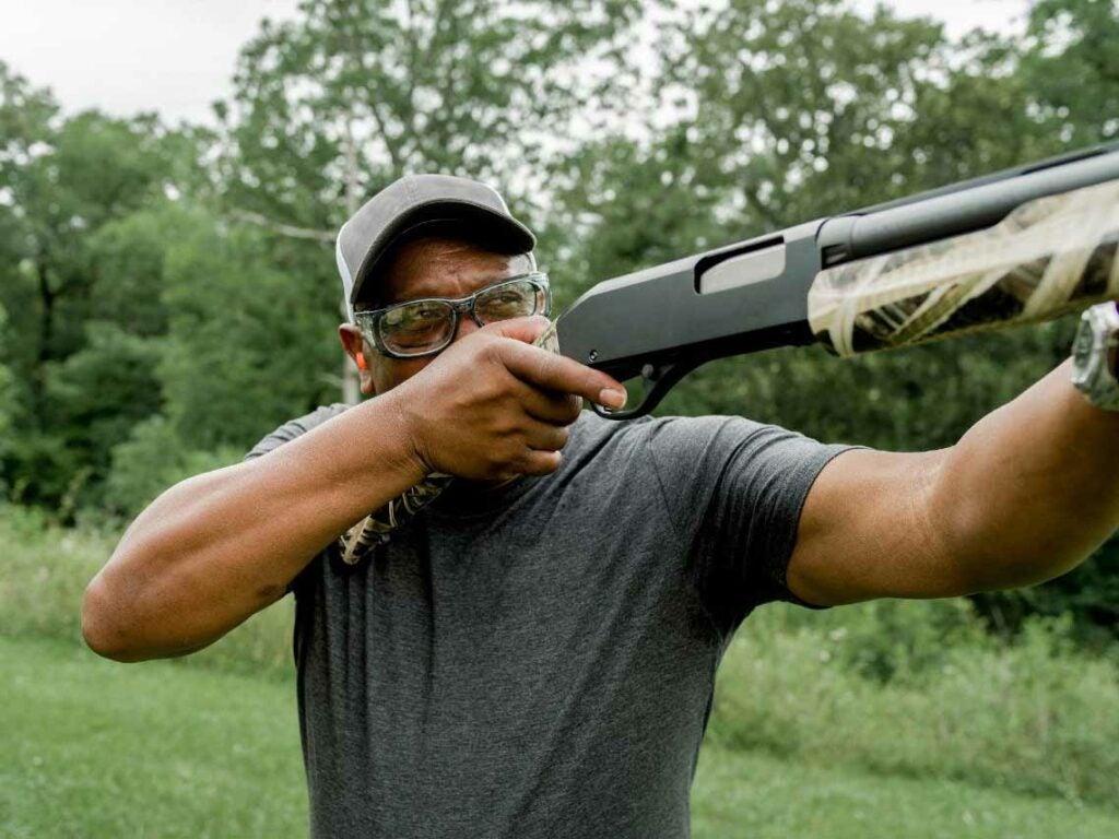 A man lifts and aims a shotgun in a shooting range.