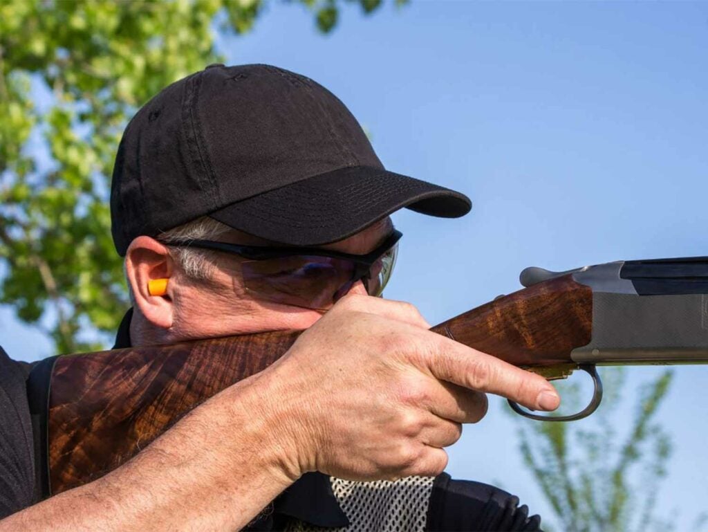 Man aiming a shotgun in a field.