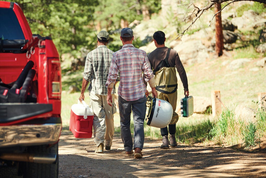 Three men walking with camping supplies.
