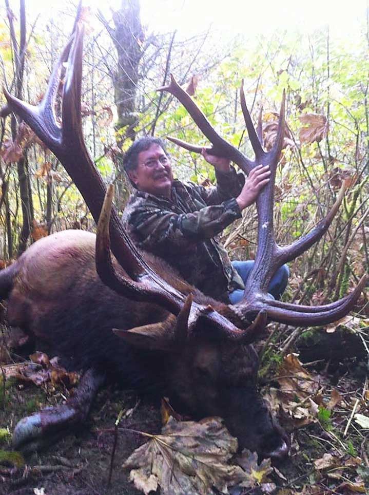A man and a trophy elk in the woods.