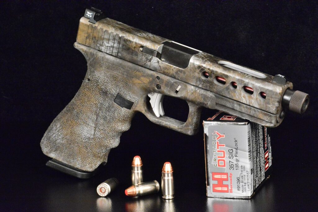 A small camoflauged handgun propped against a box of Hornady ammunition.