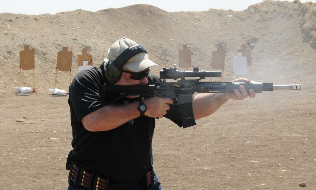 A man wearing ear and eye protection fires a rifle at a shooting range.