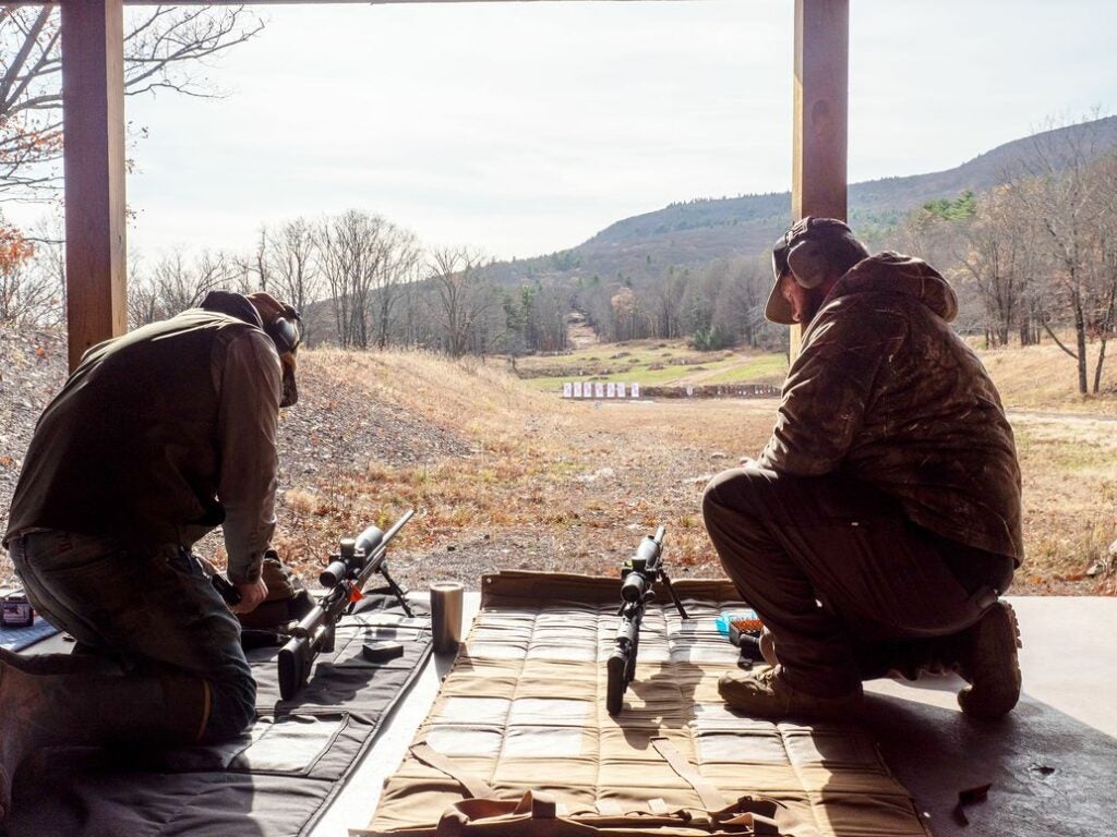 Two shooters readying their precision rifles at the firing line on an outdoor long-range course.