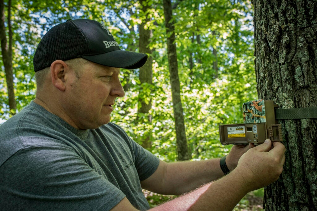 Man operating trail camera in the woods.