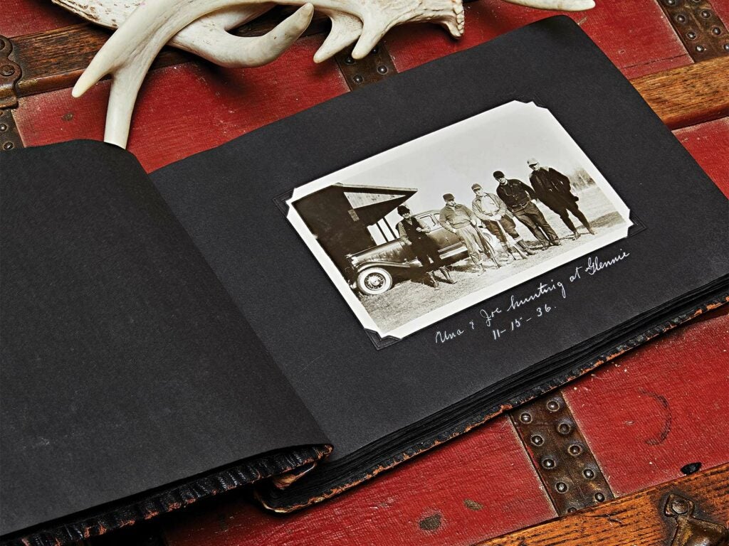 A photo album of vintage photographs on a chest with deer antlers.