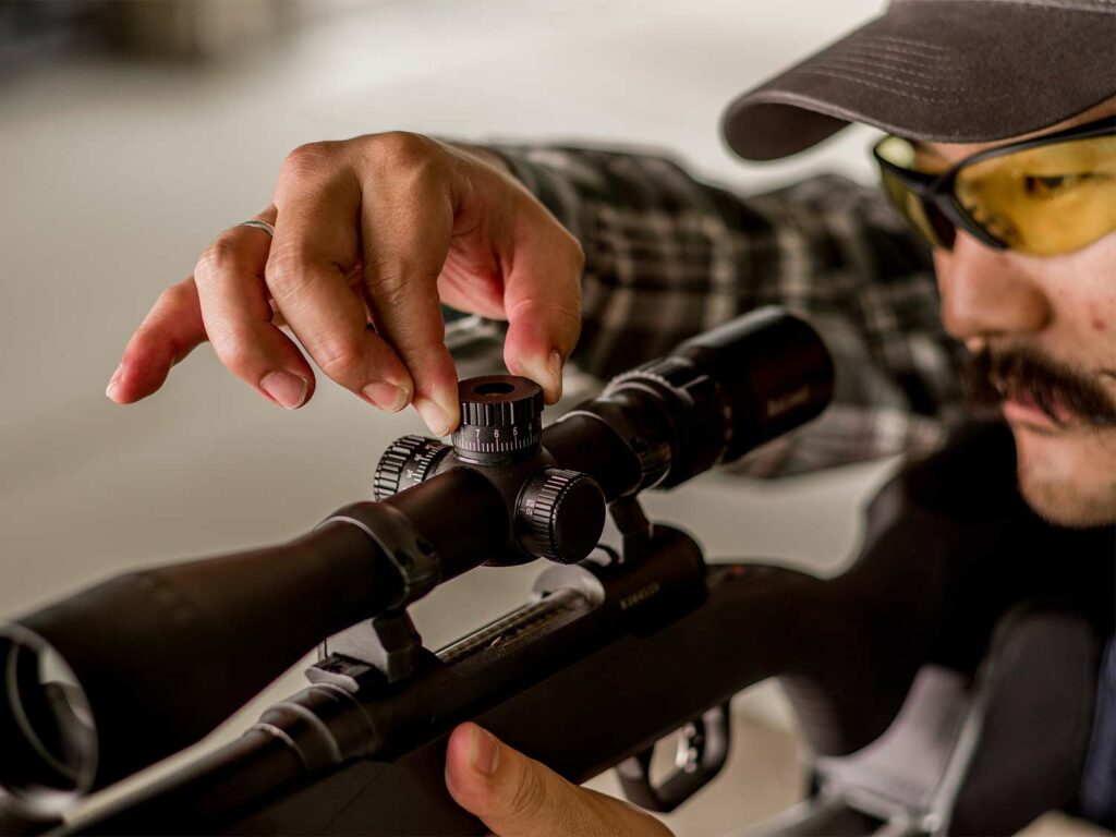 A man in shooting safety goggles adjusting a riflescope.