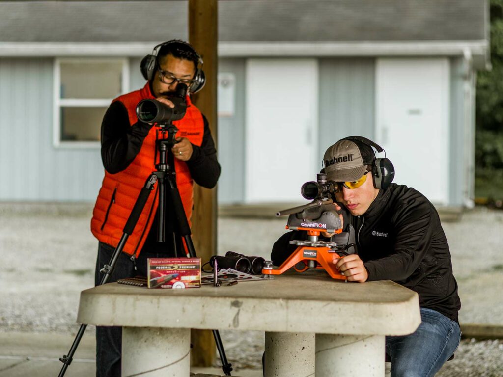 Two men adjusting riflescopes and making adjustments at a shooting range.