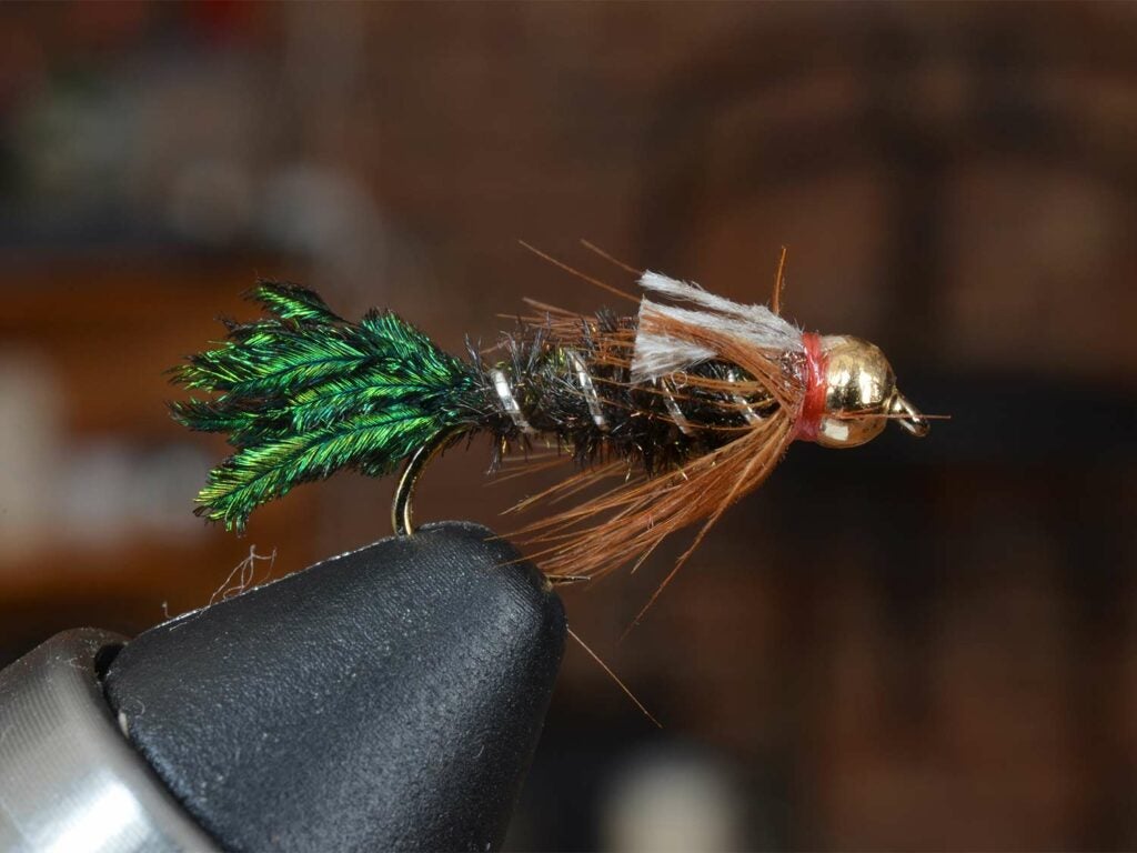 A green, copper and silver fly lure secured in a vice grip.