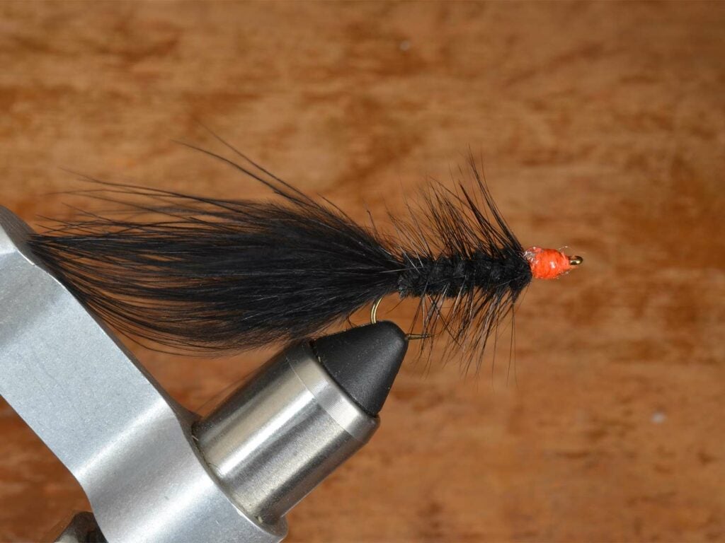 A black and orange fuzzy fly lure in a vice grip.
