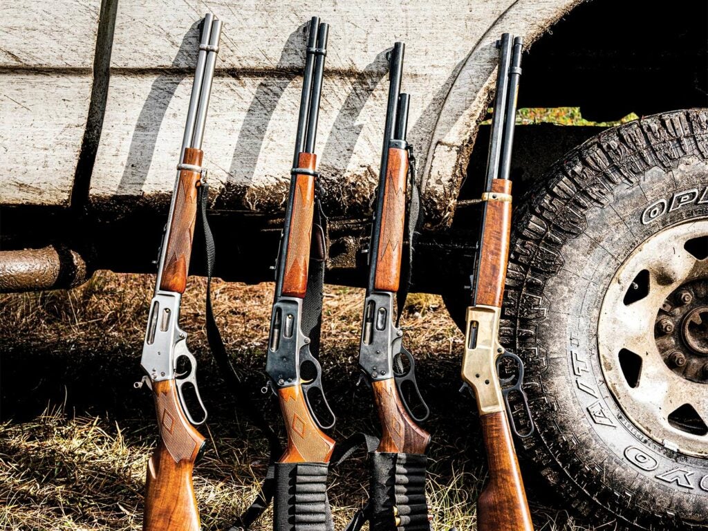 A lineup of four lever-action rifles leaning against a muddy pickup truck.