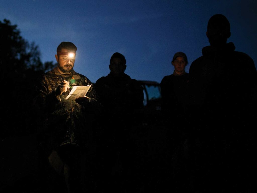 Several hunters standing outside at night with one wearing a headlamp.