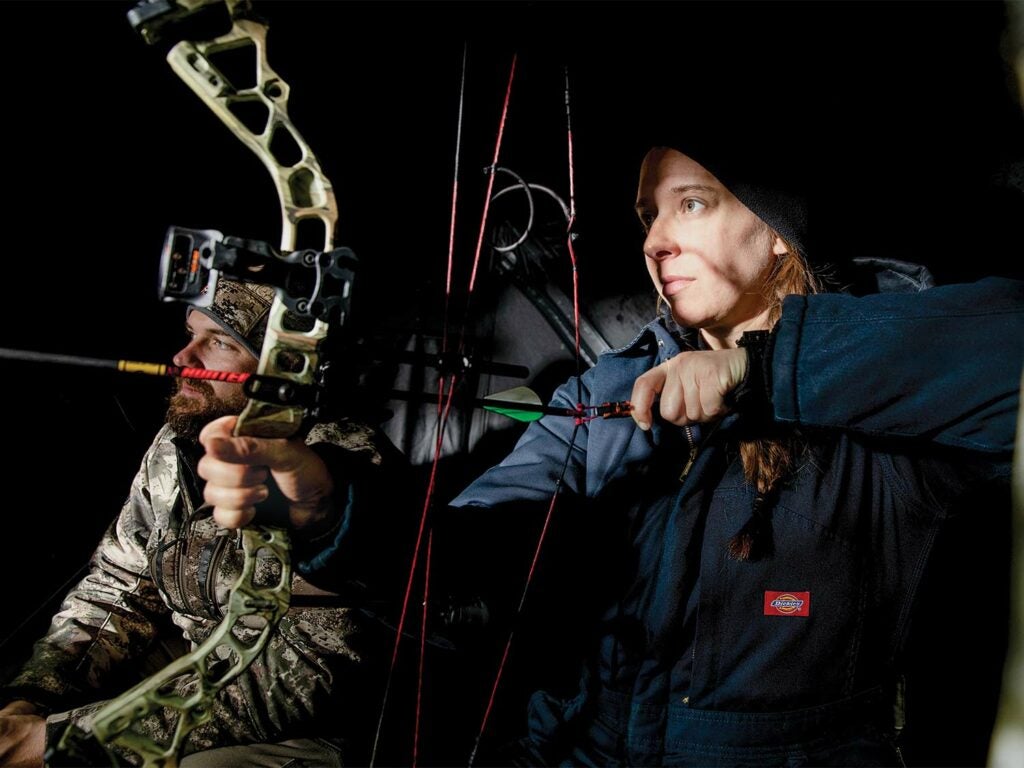 A female hunter draws back on a compound bow.