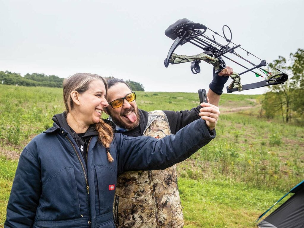 A man and woman stands in an open field while taking a selfie.