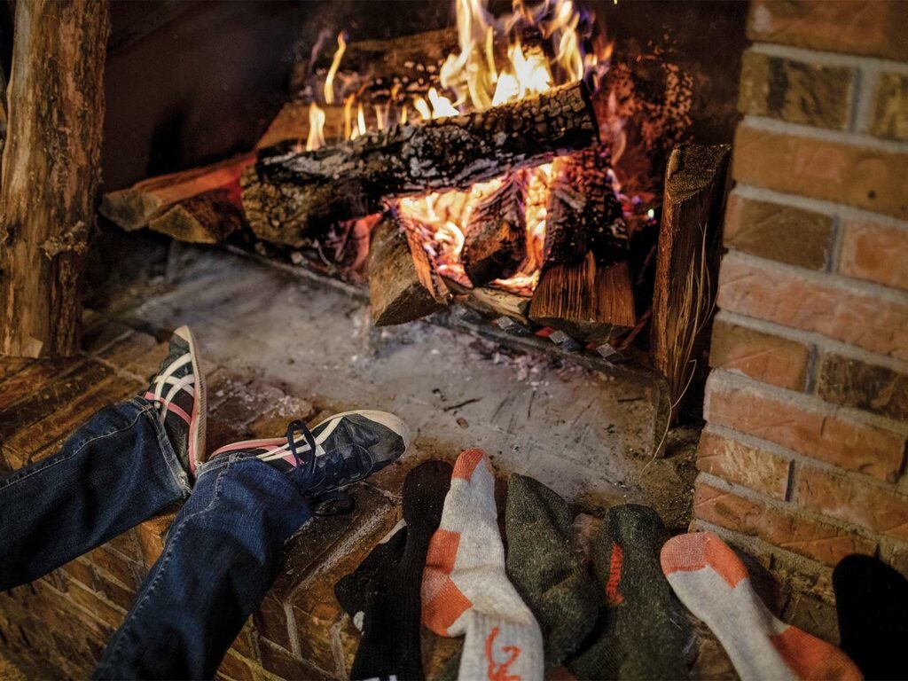 A person kicks back by the fire and leaves their socks to dry next to the fireplace.