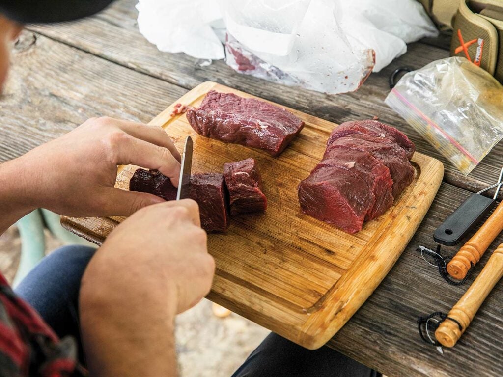 Someone slices wild game meet on a cutting board.
