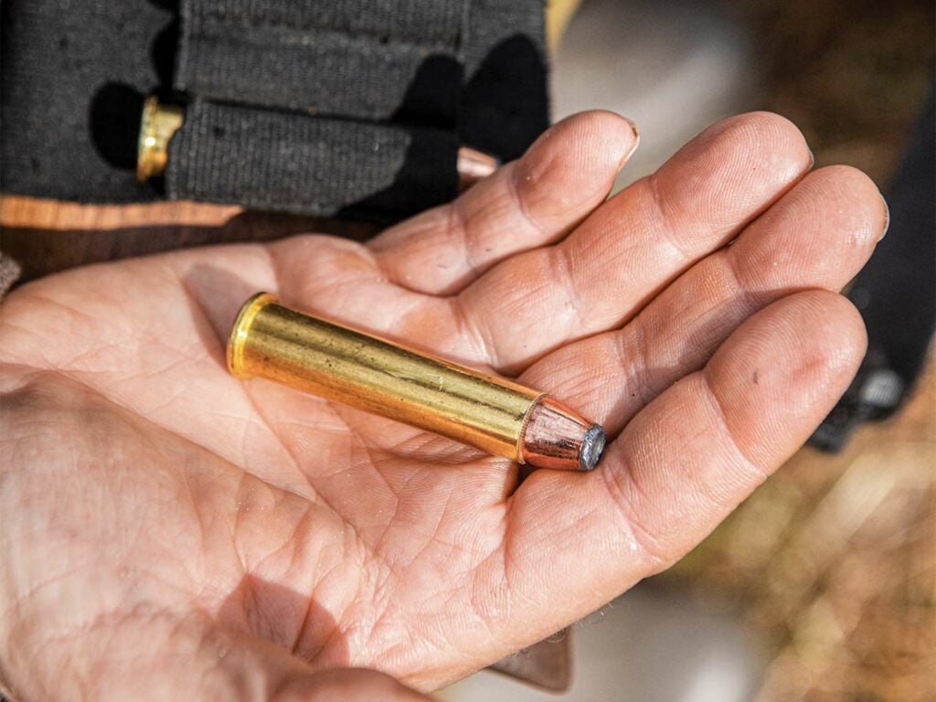 A single rifle bullet in the hand of a hunter preparing to load it into a lever-action rifle.