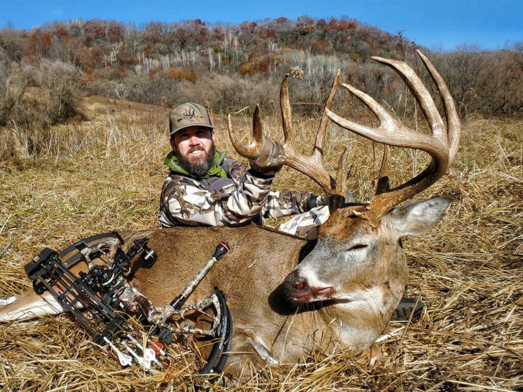 A hunter kneels behind a large buck.