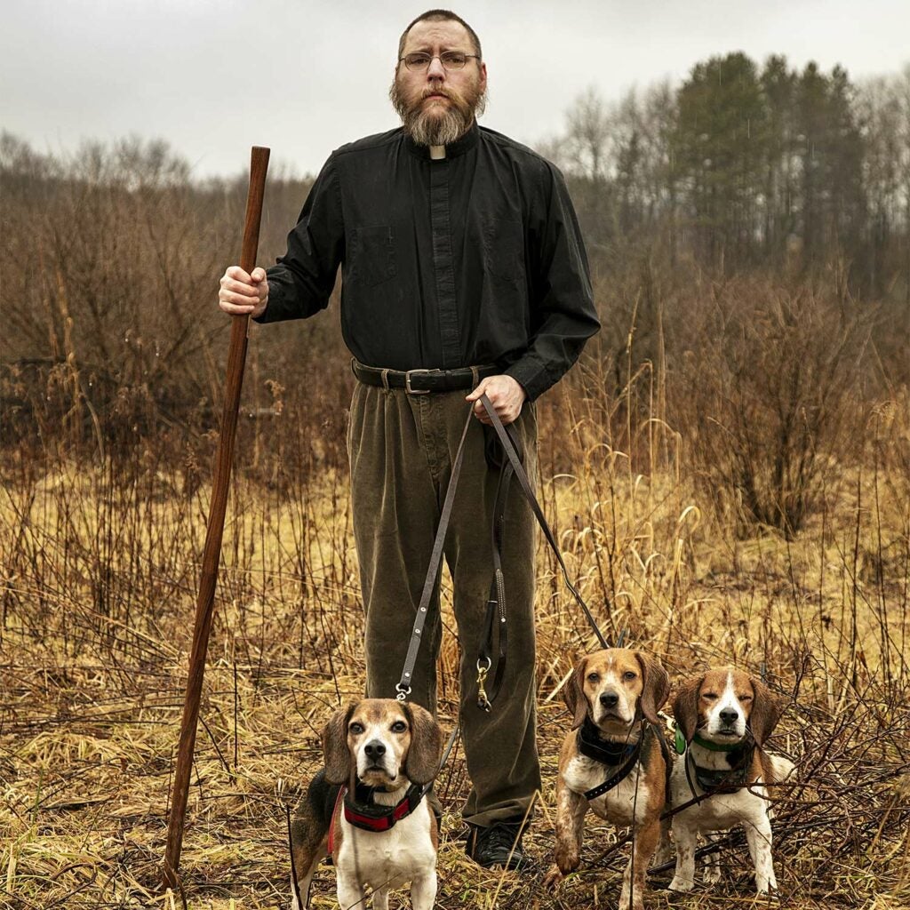 A hunter holds three beagles on a leash.